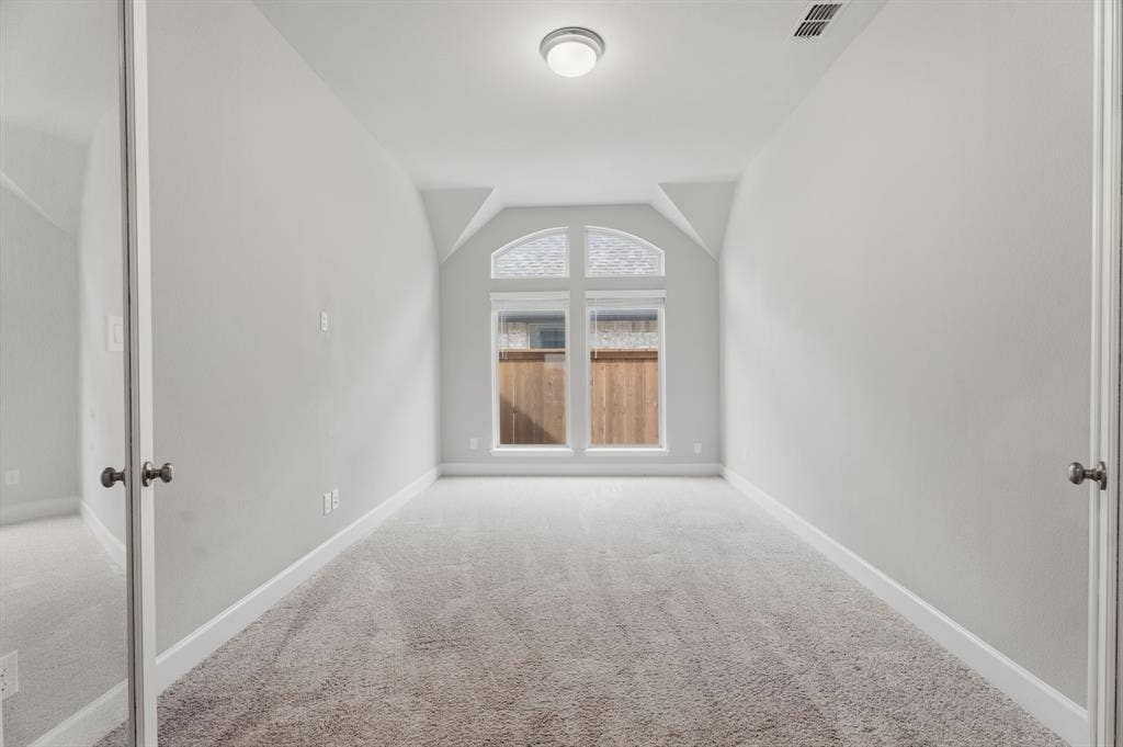 Room featuring light gray carpeting, a single ceiling light fixture, white baseboards, and a prominent arched window