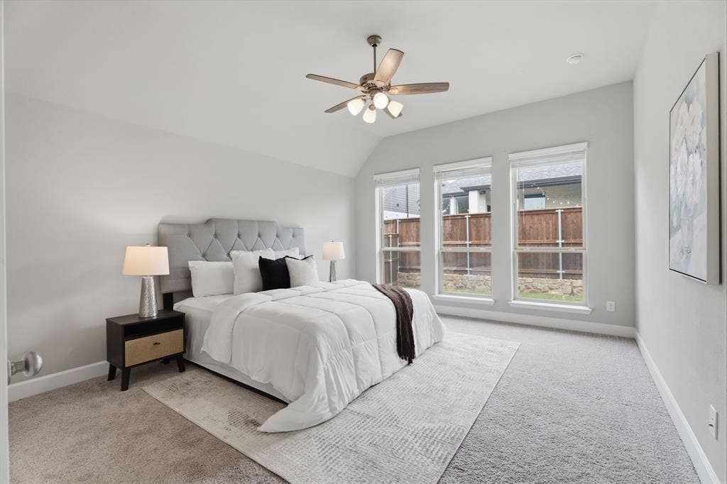 Carpeted room featuring three rectangular windows with blinds, a vaulted ceiling, and a ceiling fan with integrated lighting