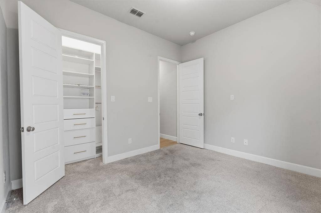 Spacious room featuring light gray walls, plush gray carpeting, and white baseboards