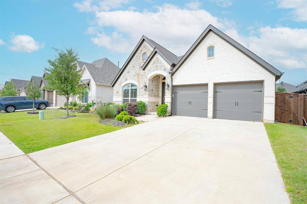 Contemporary architectural style with a brick and stone facade, a two-car garage, established landscaping, and a concrete driveway