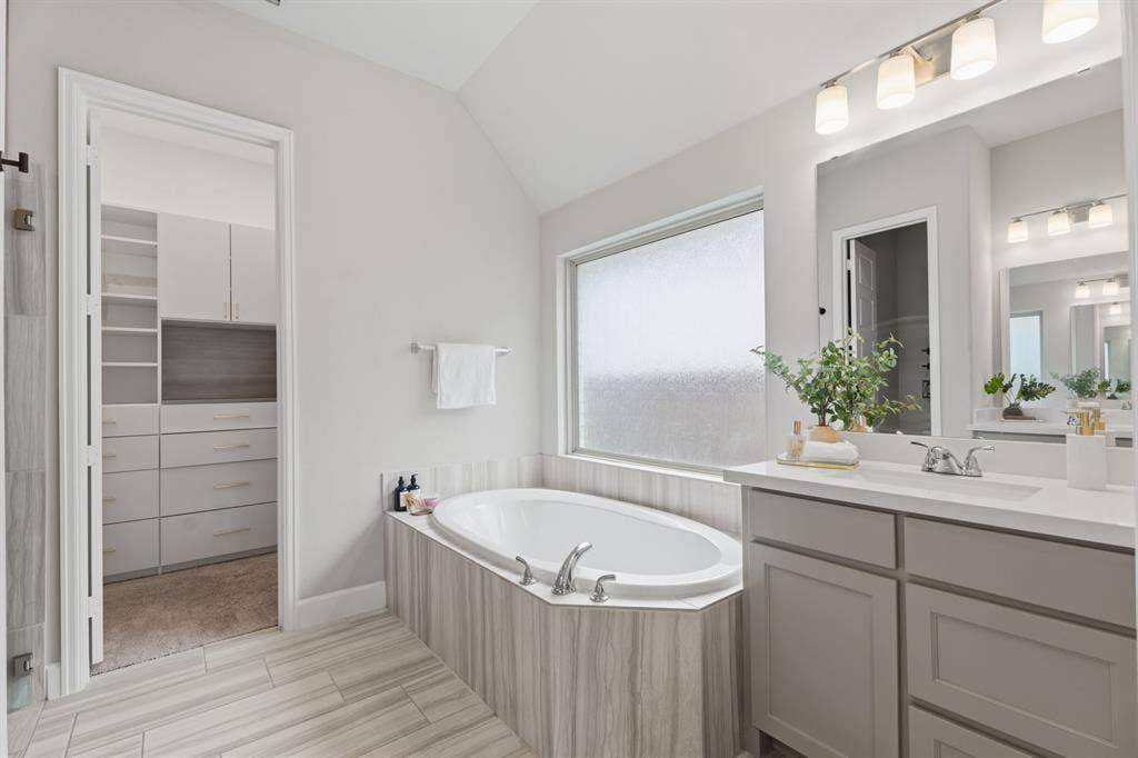 Bright bathroom featuring a large soaking tub, double vanity with quartz-finish countertop, and a spacious walk-in closet with built-in shelving