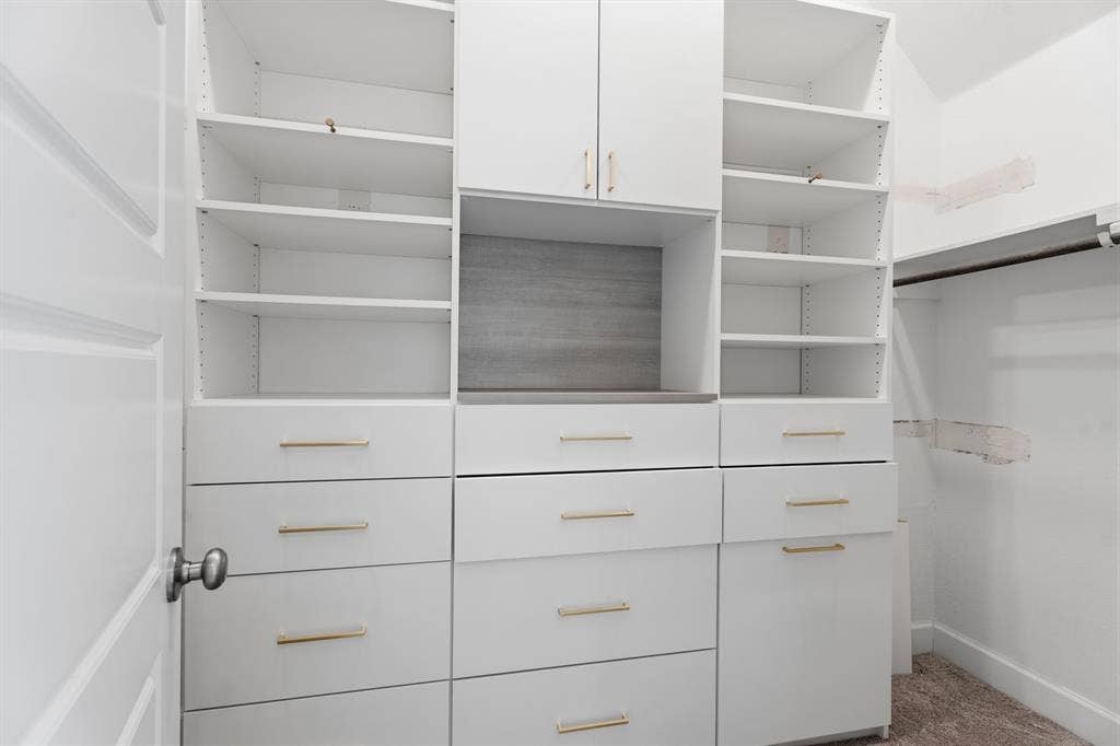 Custom white built-in closet system featuring multiple shelves, drawers with gold-tone hardware, and cabinet storage