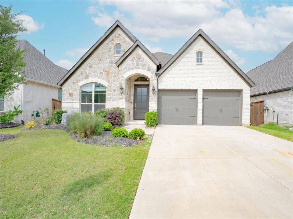 Stone and brick exterior featuring a two-car garage, arched entry, and front landscaping