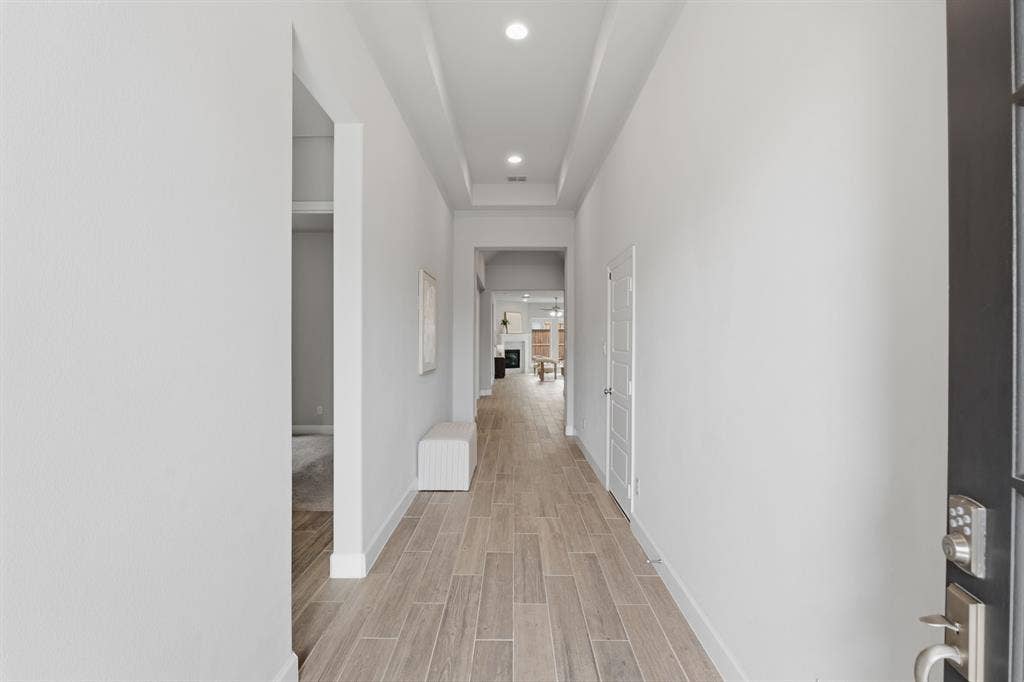 Spacious interior hallway featuring wood-finish tile flooring, recessed lighting, and a tray ceiling