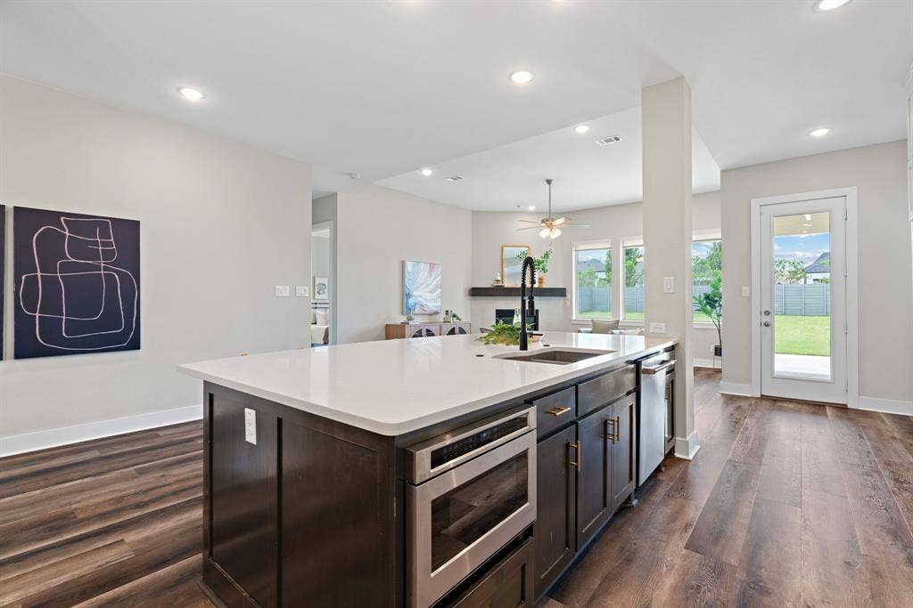 1821 Stonewall Road, Argyle, TX 76226 Kitchen island featuring a white countertop, undermount sink with a black gooseneck faucet, built-in microwave, and dark wood cabinetry
