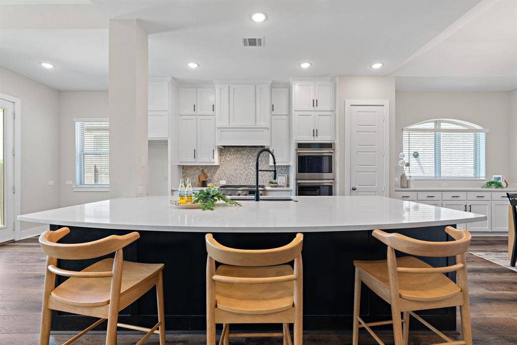 1821 Stonewall Road, Argyle, TX 76226 Expansive kitchen island with a light-toned countertop and black base, complemented by white cabinetry and stainless steel double ovens
