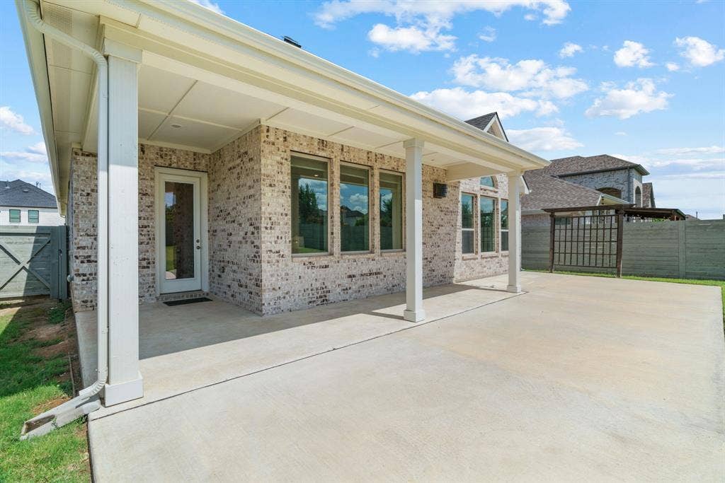 1821 Stonewall Road, Argyle, TX 76226 Expansive concrete patio beneath a covered porch, featuring a brick exterior, multiple windows, and a glass-paneled door