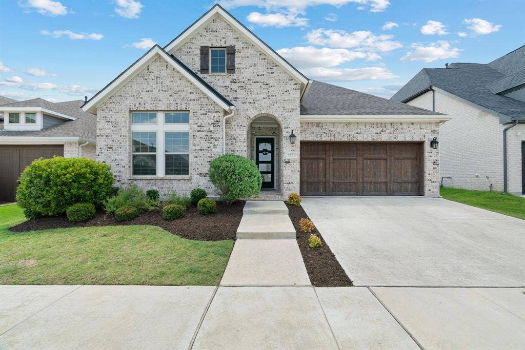 1821 Stonewall Road, Argyle, TX 76226 Brick facade residence with a dark wood-finish garage door, arched entryway, a composition shingle roof, and a concrete driveway