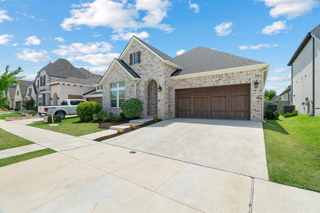 1821 Stonewall Road, Argyle, TX 76226 Brick exterior with a dark shingle roof, arched entryway, and a wood-look garage door