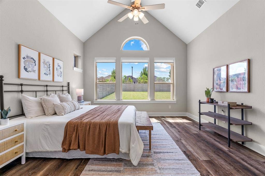 1821 Stonewall Road, Argyle, TX 76226 Vaulted ceiling bedroom featuring wood-finish flooring, a ceiling fan, and a transom window above a triple-pane window overlooking a fenced backyard