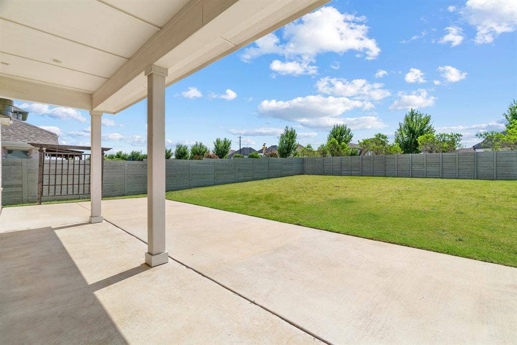 1821 Stonewall Road, Argyle, TX 76226 Expansive concrete patio with a covered outdoor living area and a large grassy backyard featuring mature trees and a privacy fence