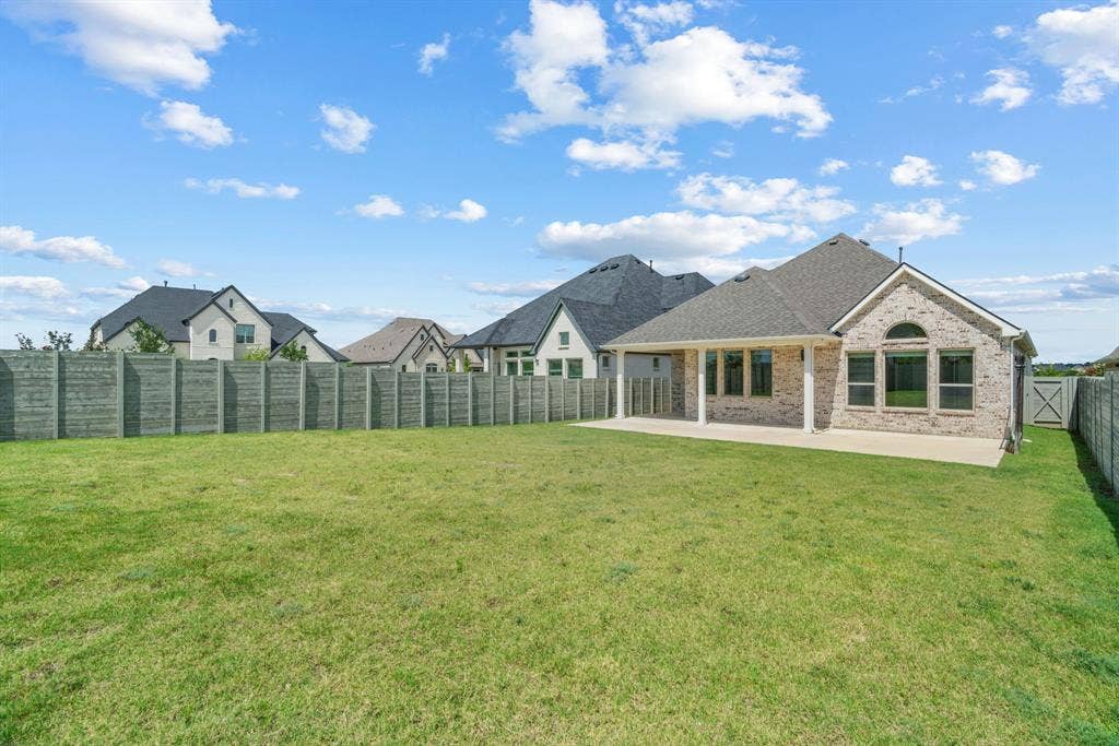 1821 Stonewall Road, Argyle, TX 76226 Expansive backyard featuring a large green lawn, a covered patio, and a light brick exterior with a dark shingled roof