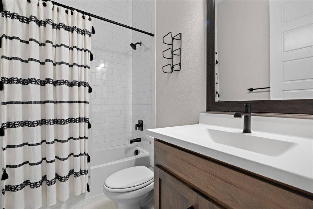 1821 Stonewall Road, Argyle, TX 76226 Bathroom featuring a white subway tile tub surround, dark wood-finish vanity with a white countertop, and a rectangular undermount sink