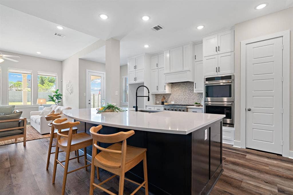 1821 Stonewall Road, Argyle, TX 76226 Contemporary kitchen featuring a large island with a light-colored countertop, white cabinetry, built-in stainless steel double ovens, and wood-finish flooring