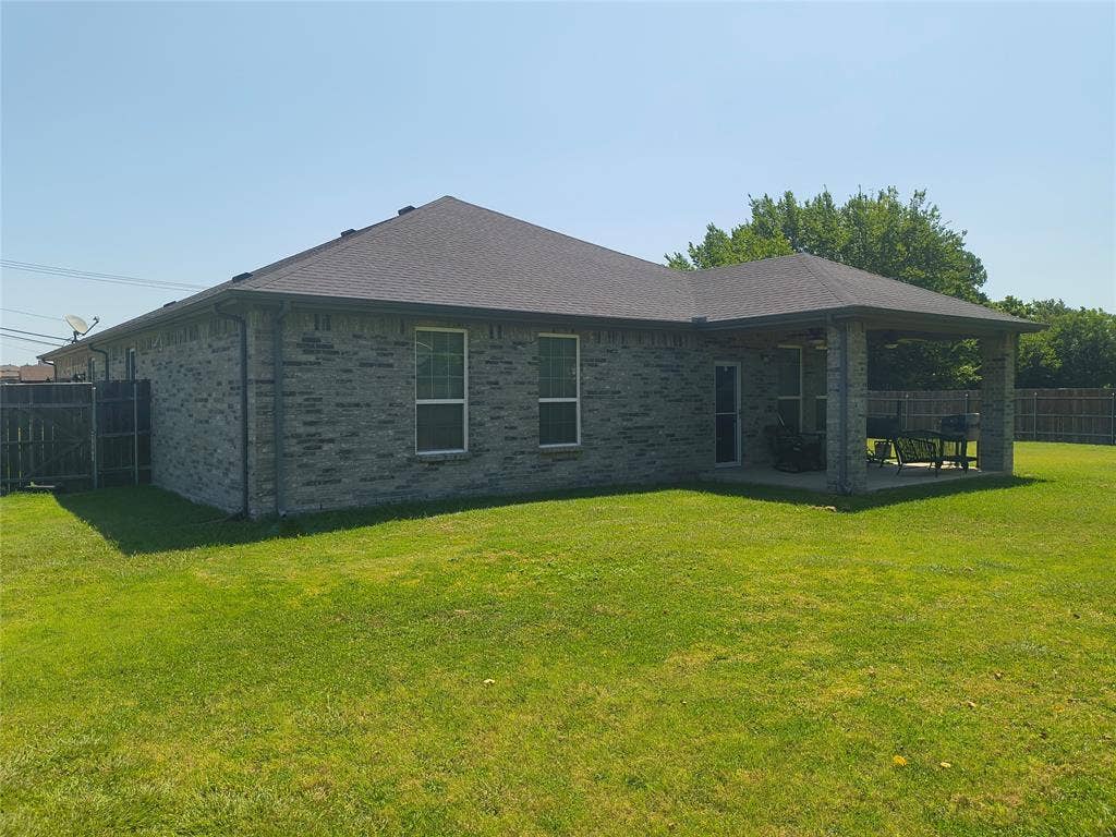 3027 Ames Road, Lancaster, TX 75134 Expansive backyard featuring a covered patio with a concrete slab, durable brick exterior, and a dark shingle roof