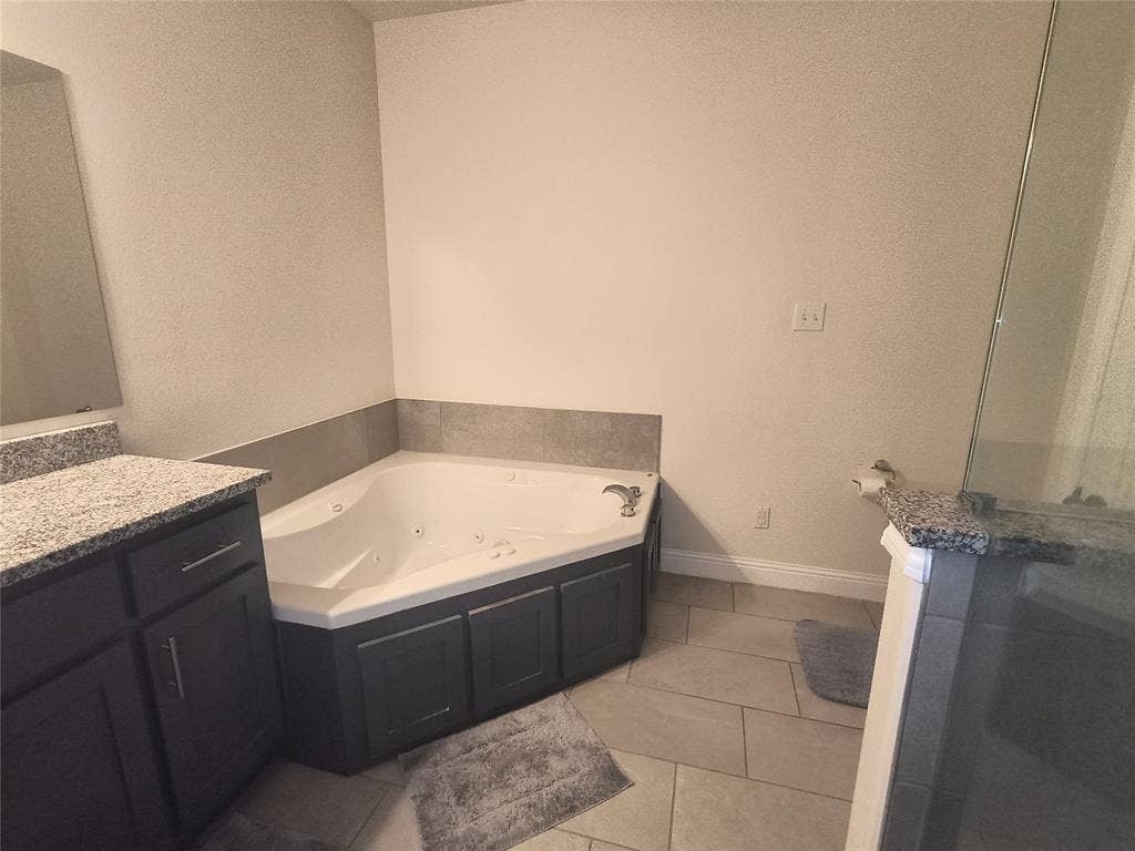 3027 Ames Road, Lancaster, TX 75134 Corner jetted tub with dark cabinetry surround, tile flooring, and a granite-topped vanity