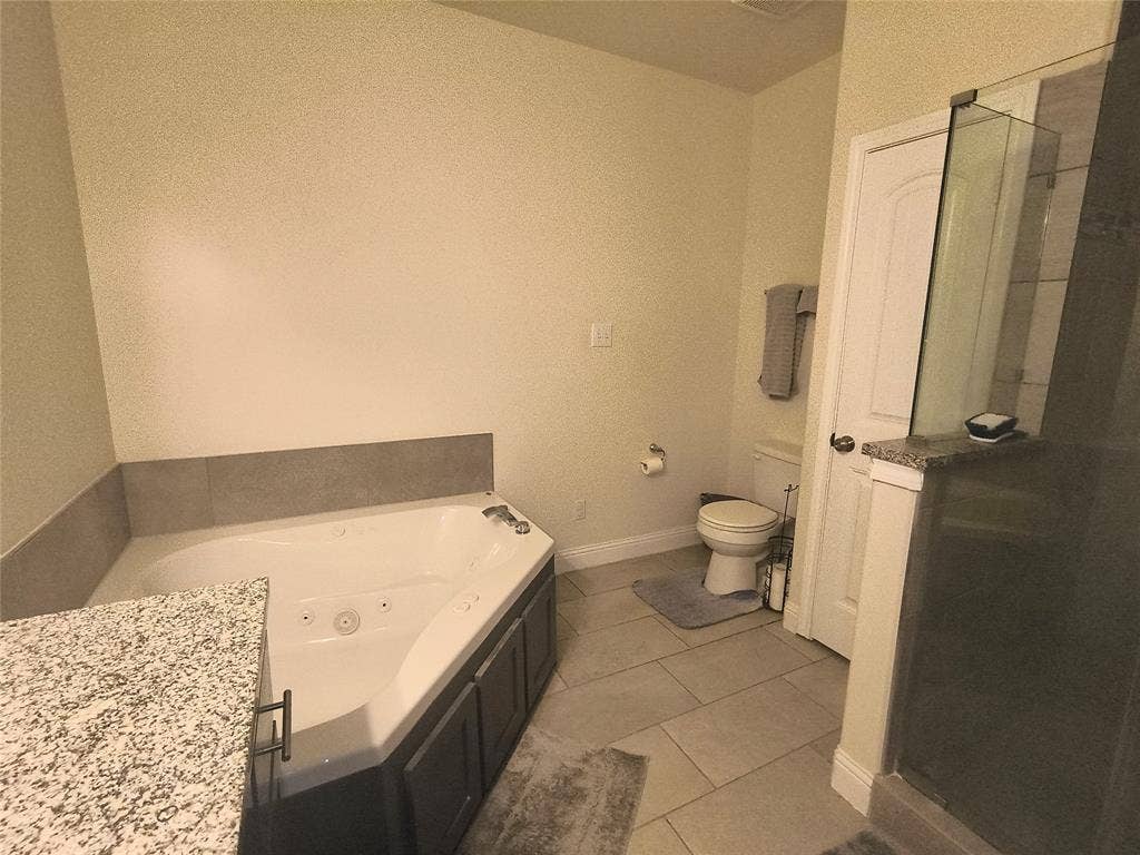3027 Ames Road, Lancaster, TX 75134 Spa-inspired bathroom featuring a corner jetted bathtub, a separate shower with glass enclosure, granite-finish countertops, and large format tile flooring