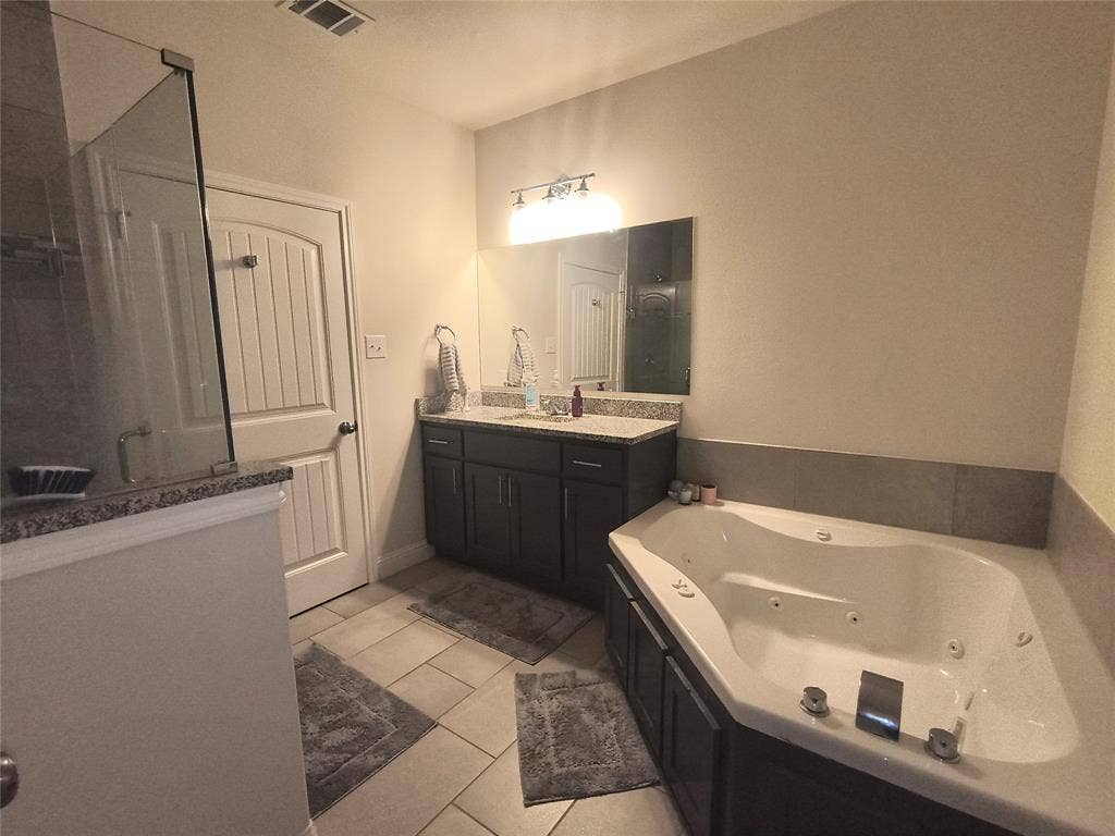 3027 Ames Road, Lancaster, TX 75134 Bathroom featuring a corner jetted soaking tub, a dark wood-finish vanity with a light-toned countertop, a frameless mirror, and a glass-enclosed shower