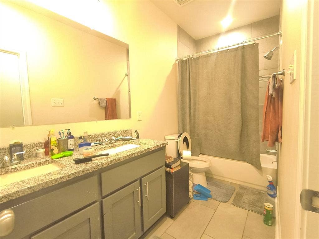 3027 Ames Road, Lancaster, TX 75134 Bathroom featuring a dual-sink vanity with a granite-style countertop, gray cabinetry, a tub/shower combination with subway tile surround, and light-toned floor tile