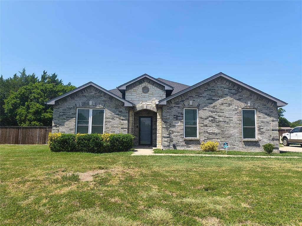 3027 Ames Road, Lancaster, TX 75134 Single-story residence featuring a gray brick exterior with light stone accents, dark-framed windows, and a dark shingle roof