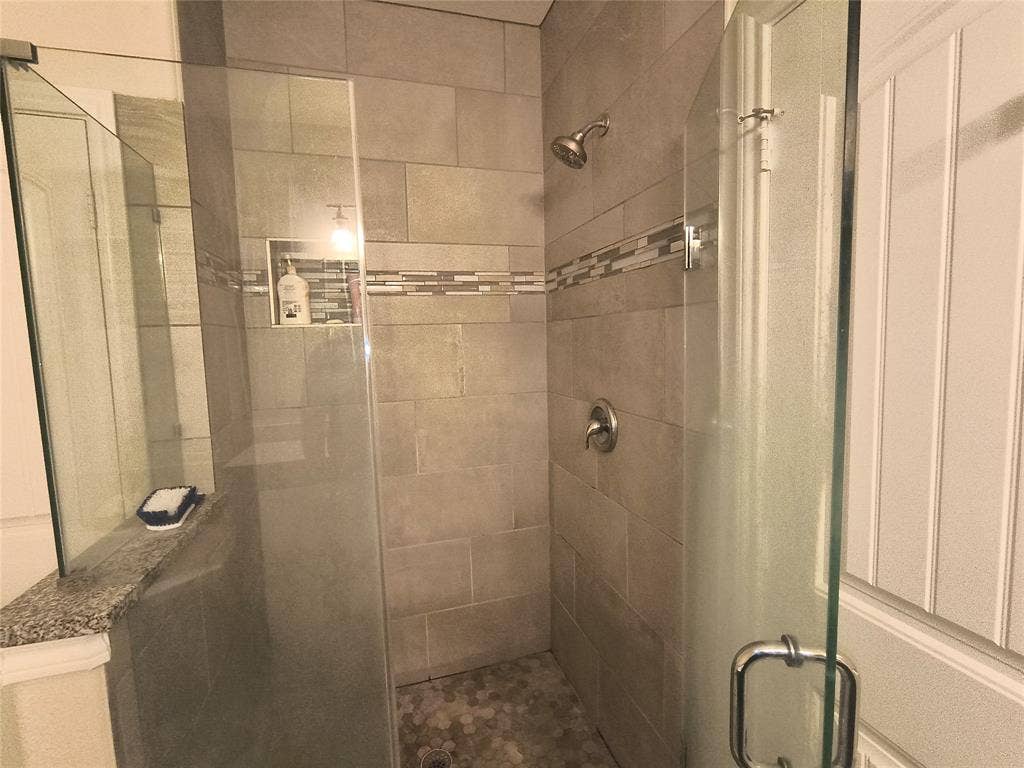 3027 Ames Road, Lancaster, TX 75134 Shower enclosure with clear glass panels, subway-style wall tiling, mosaic accent band, built-in recessed shelf, and hexagonal floor tiling