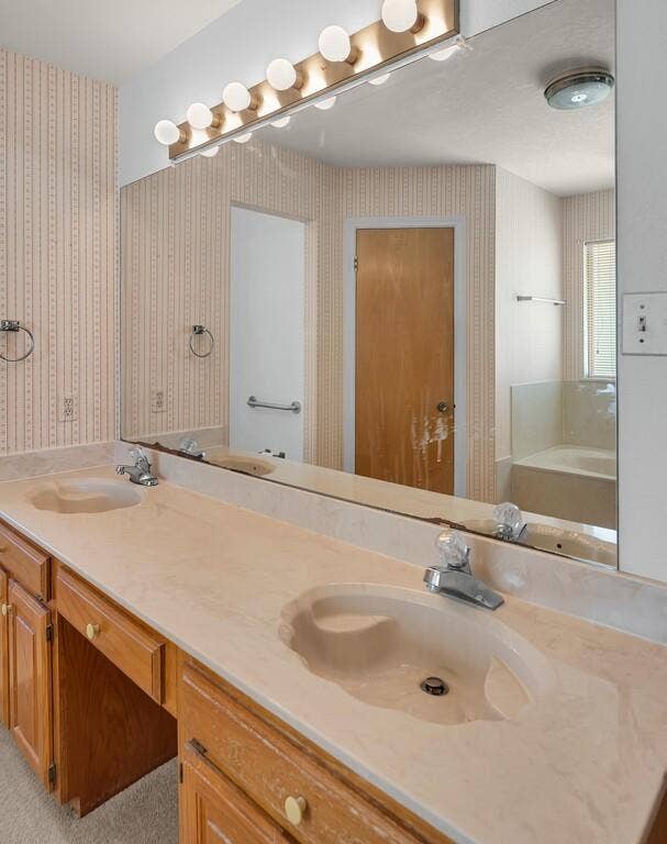 600 Lyndon Drive, Woodway, TX 76712 Spa-inspired master bathroom featuring a dual-sink vanity with wood cabinetry, cream-colored countertop with integral basin design, and chrome faucet fixtures