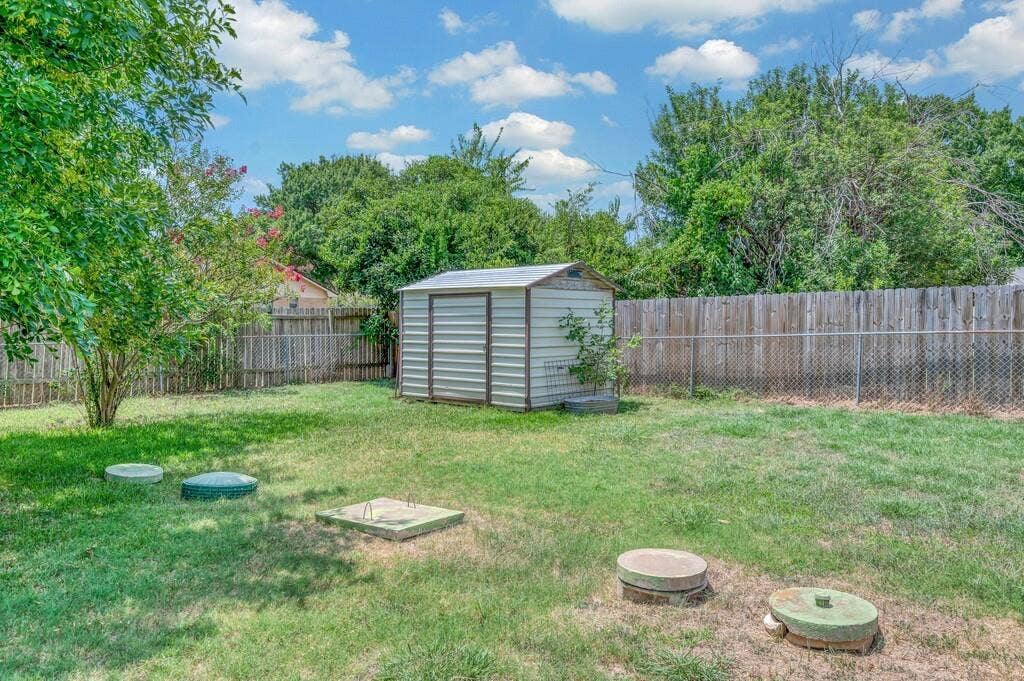 600 Lyndon Drive, Woodway, TX 76712 Spacious backyard featuring a storage shed with a metal roof, mature trees, and a combination of wood and chain-link fencing