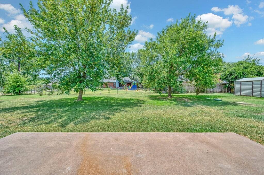 600 Lyndon Drive, Woodway, TX 76712 Expansive backyard featuring a concrete patio, mature trees, a manicured lawn, a wood fence, and a metal storage shed