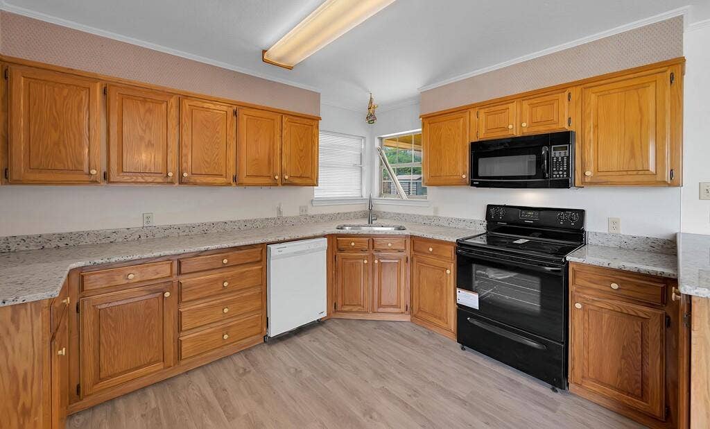 600 Lyndon Drive, Woodway, TX 76712 Kitchen featuring wood cabinetry, light-toned countertops, a stainless steel sink, and black appliances including a range and microwave
