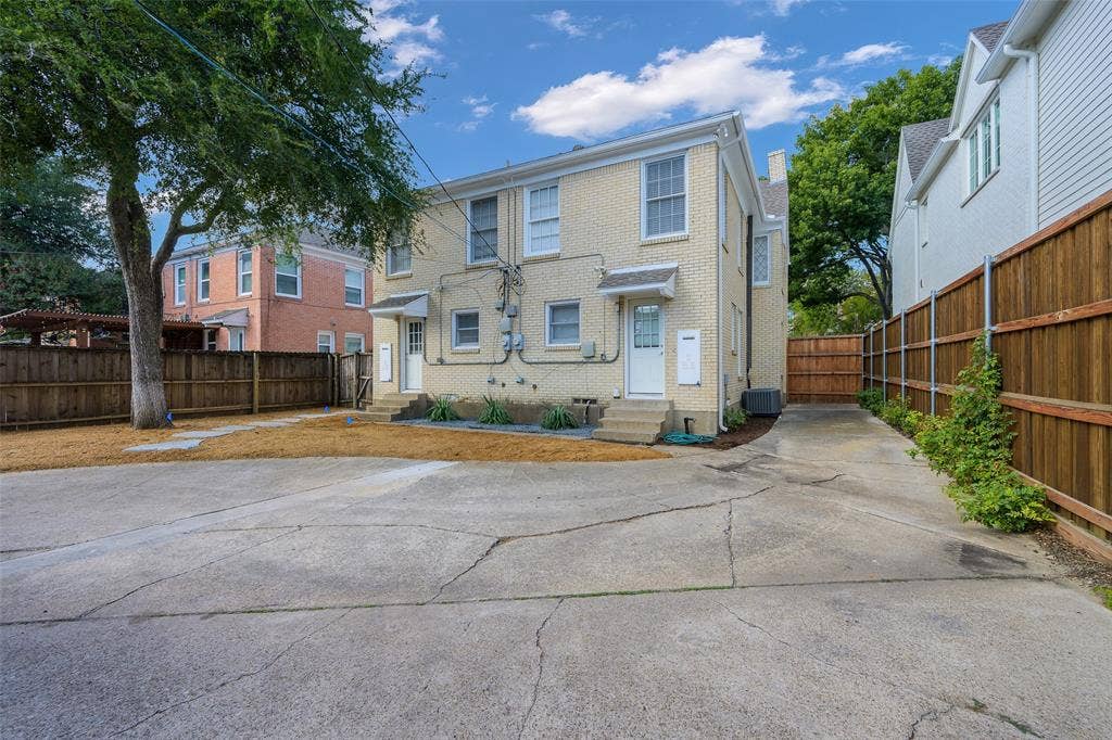 Exterior featuring light-colored brick siding, concrete parking area, and wood privacy fencing