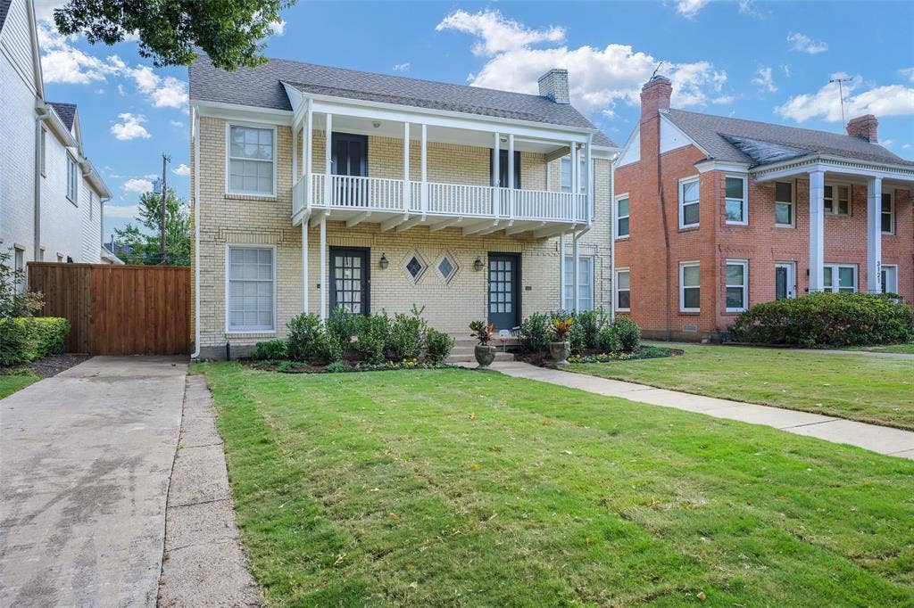 Two-story brick exterior featuring a second-level balcony with railings, double front entry doors, diamond-shaped accent windows, and a paved private driveway