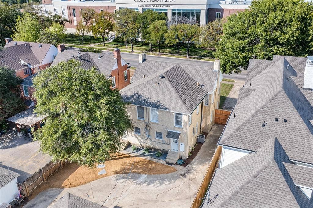 Two-story exterior featuring light-toned masonry, a multi-gabled roof, mature landscaping, and a paved driveway