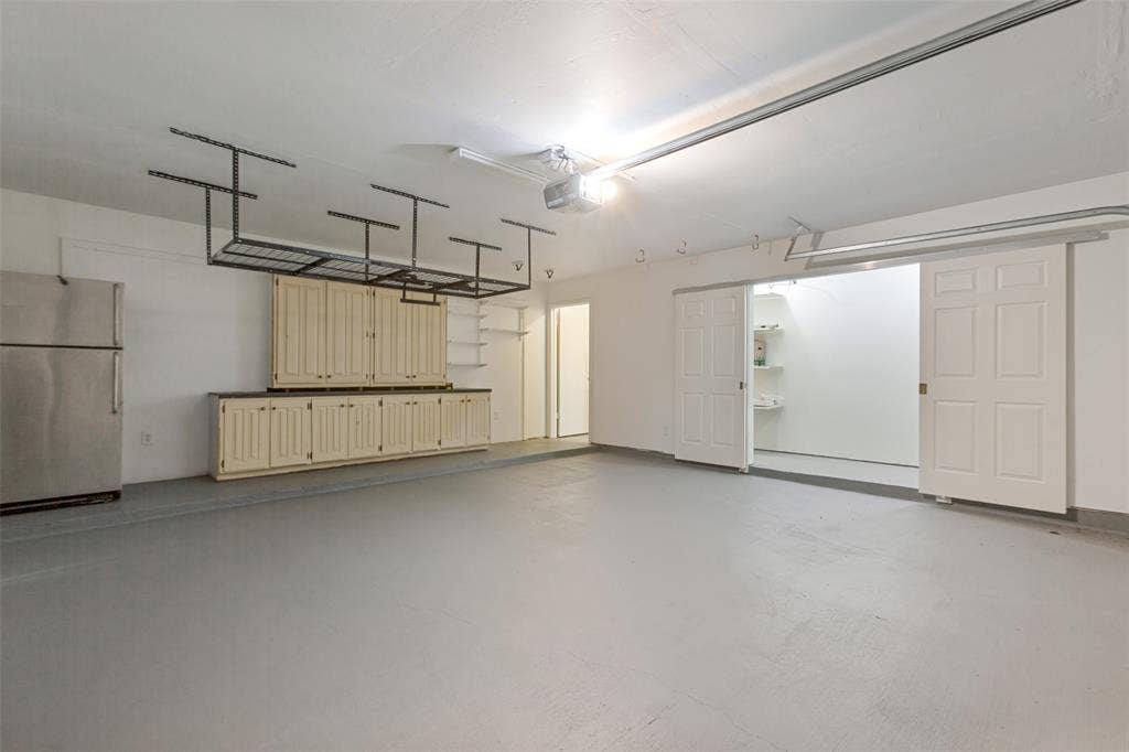 6362 Southpoint Drive, Dallas, TX 75248 Spacious garage featuring freshly painted flooring, custom wood-finish cabinetry with ample storage, integrated ceiling-mounted organization system, and recessed lighting throughout