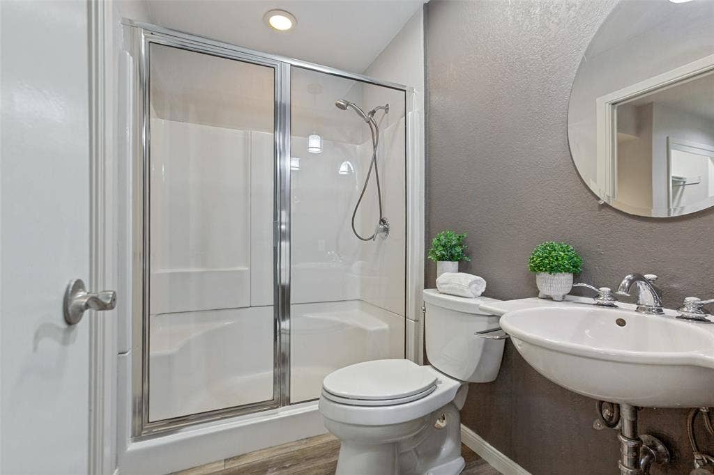6362 Southpoint Drive, Dallas, TX 75248 Glass-enclosed shower with white surround, recessed lighting, wall-mounted sink with chrome faucet, and wood-finish flooring
