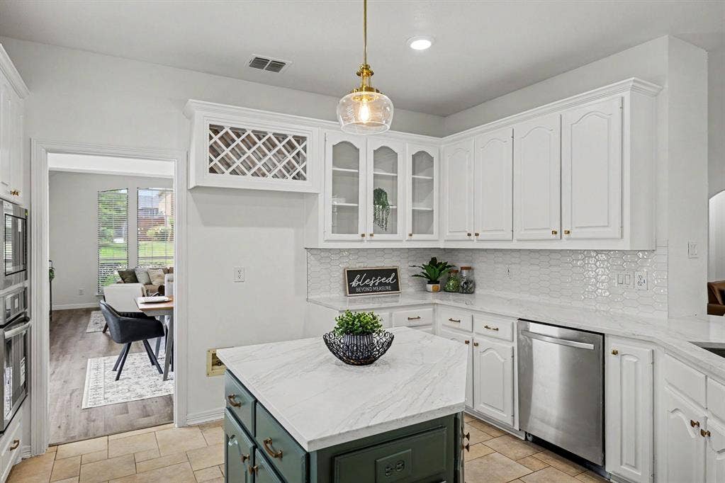 7904 Alderwood Place, Plano, TX 75025 Kitchen featuring an island with a light-toned countertop, white cabinetry with gold-toned hardware, a white hexagonal tile backsplash, and stainless steel appliances