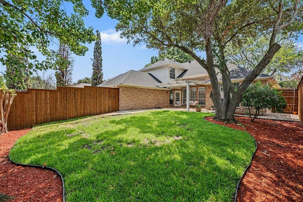 7904 Alderwood Place, Plano, TX 75025 Expansive fenced backyard featuring a manicured lawn, established shade trees, and a mulched perimeter