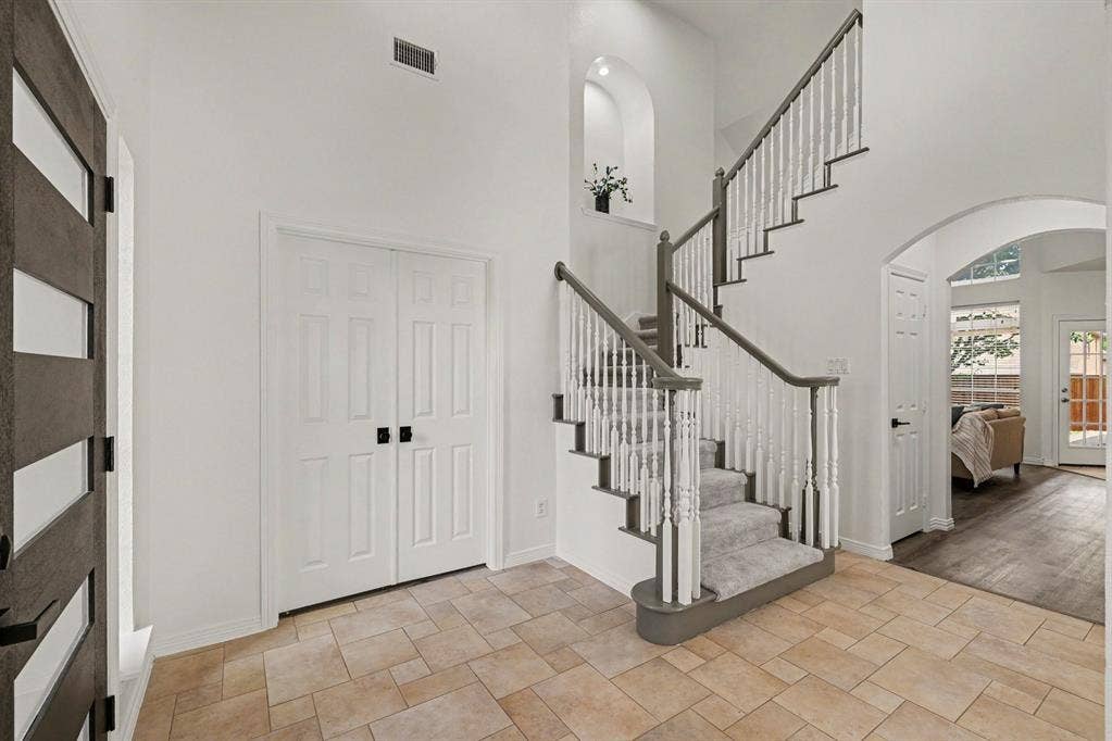 7904 Alderwood Place, Plano, TX 75025 Gracious foyer featuring a carpeted staircase with painted spindles and dark handrails, arched entryway, and neutral tile flooring