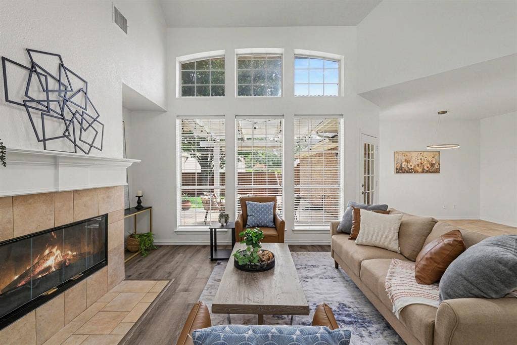 7904 Alderwood Place, Plano, TX 75025 Living area featuring a floor-to-ceiling tiled fireplace, large windows with arch-top transoms, wood-finish flooring, and a vaulted ceiling