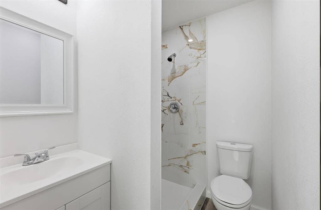 810 N Carrier Parkway, Grand Prairie, TX 75050 Compact bathroom featuring a white vanity with integrated sink, framed mirror, and a shower with white and gold veined tile surround
