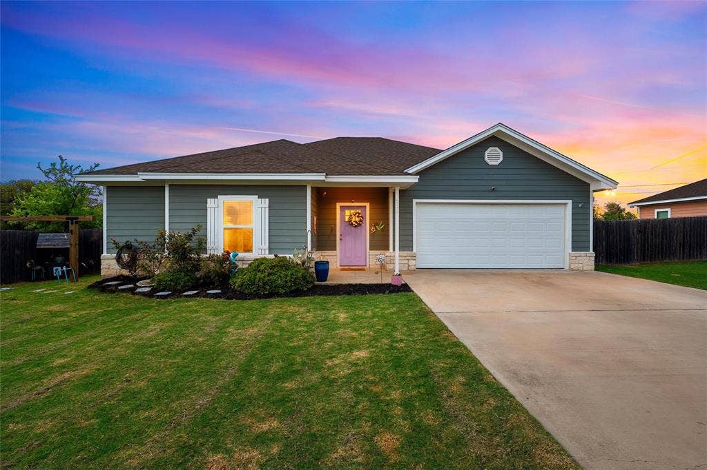 215 Greenbriar Street, Robinson, TX 76706 Single-story residence featuring horizontal siding, a light purple entry door, a stone facade accent, a covered front porch, and an attached two-car garage