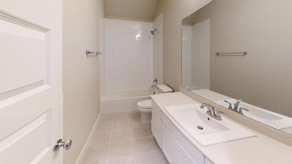 1323 Great Sand Dune Street, Royse City, TX 75189 Bathroom featuring a white vanity with an integrated sink, polished chrome faucet, a large wall-mounted mirror, a white bathtub with a tiled shower surround, and neutral-toned tile flooring