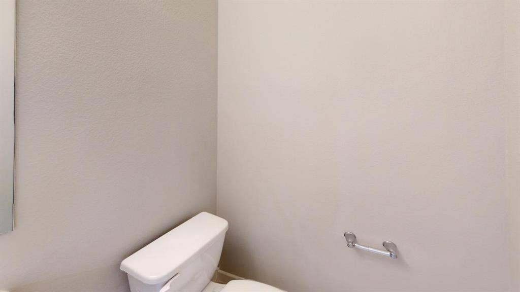 1323 Great Sand Dune Street, Royse City, TX 75189 White toilet with a wall-mounted chrome toilet paper holder and a partially visible mirror