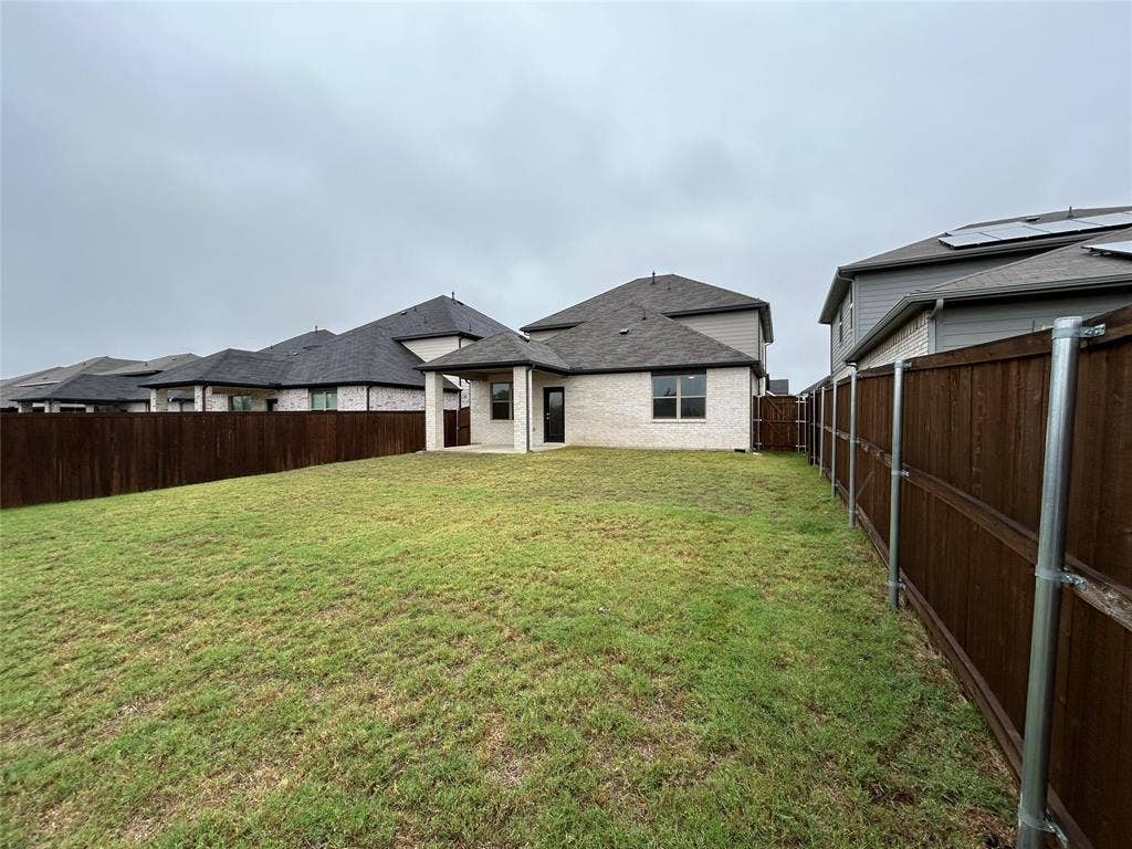 1323 Great Sand Dune Street, Royse City, TX 75189 Expansive backyard featuring a manicured lawn, full privacy fencing, a covered patio, and light brick exterior