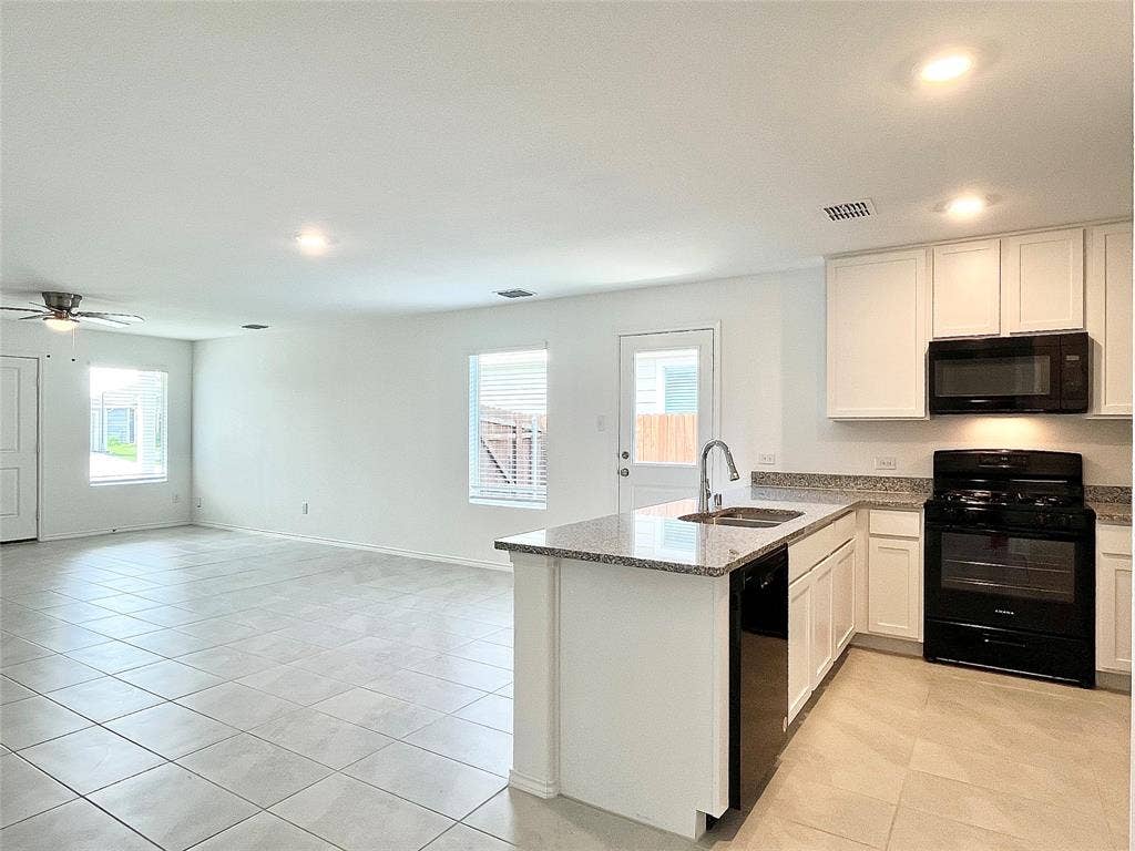 7212 Gray Wolf Lane, McKinney, TX 75071 Kitchen with black appliances, a peninsula, open floor plan, light stone counters, and plenty of natural light