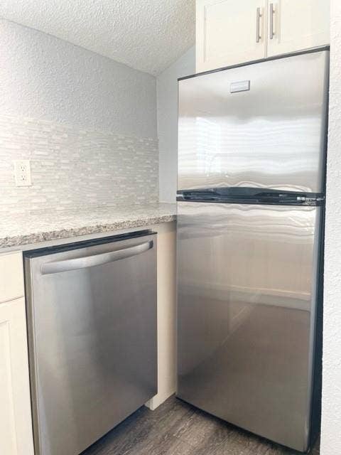 Kitchen featuring stainless steel appliances, white cabinetry with silver hardware, speckled countertops, and a mosaic tile backsplash