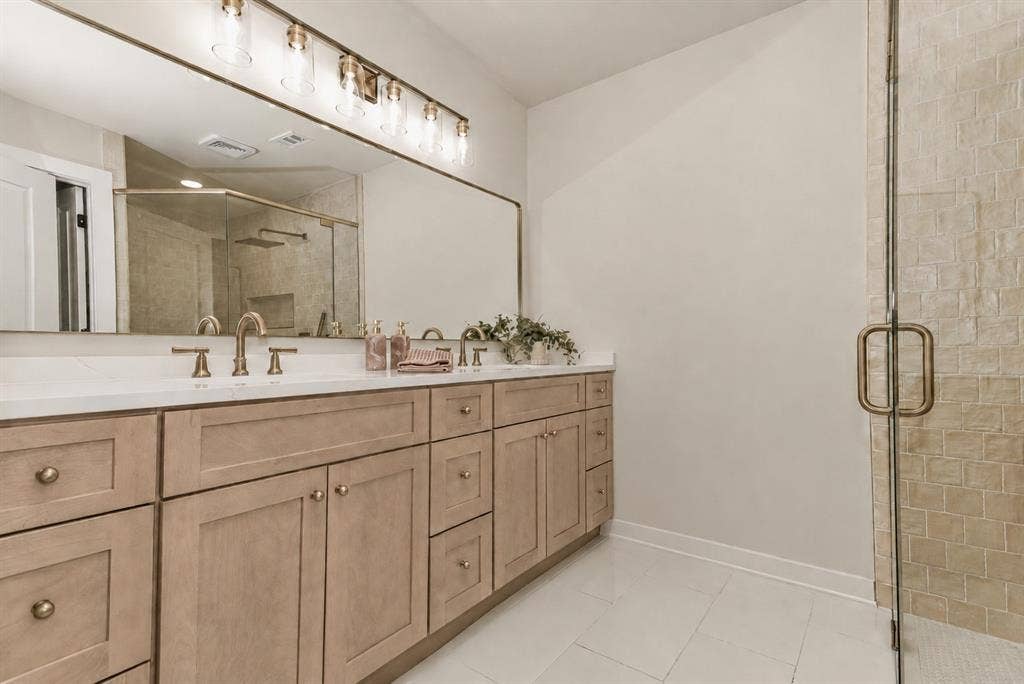 Double vanity with light wood-finish cabinetry, white countertop, and gold-finish fixtures