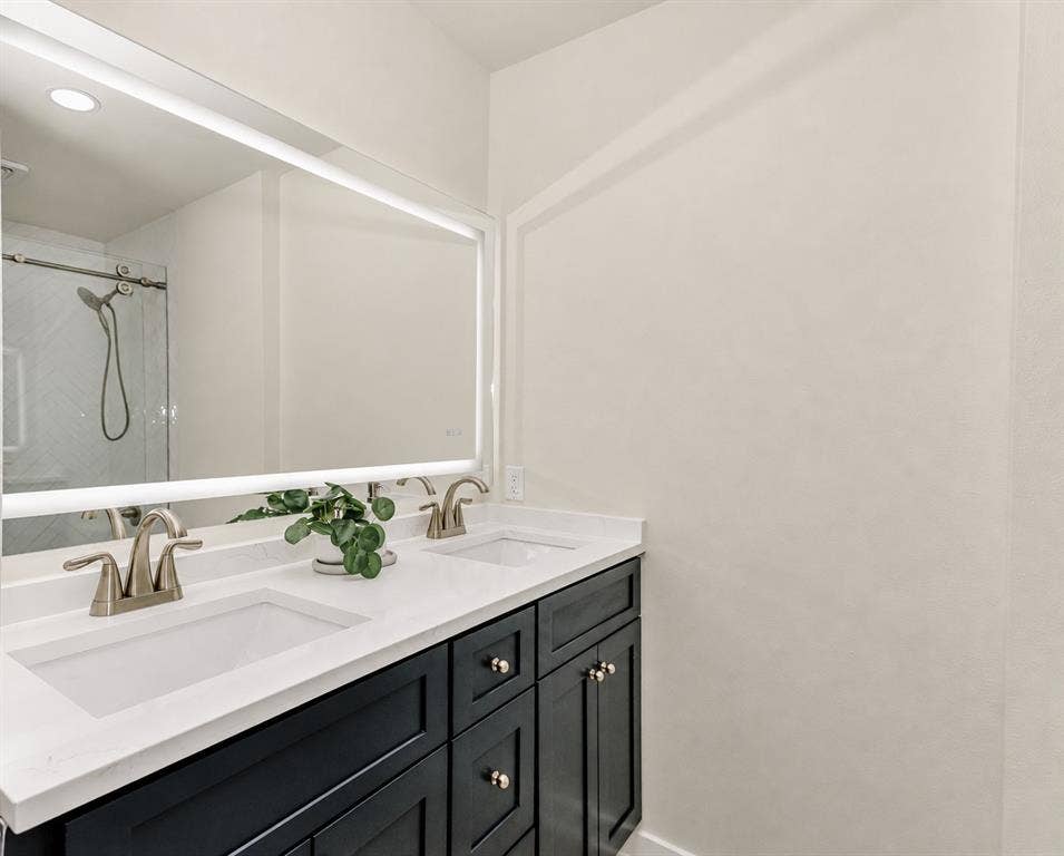 Ensuite Bath for the 2nd Bedroom. Dual vanity with integrated sinks, white countertops, dark wood-finish cabinetry, and an illuminated mirror