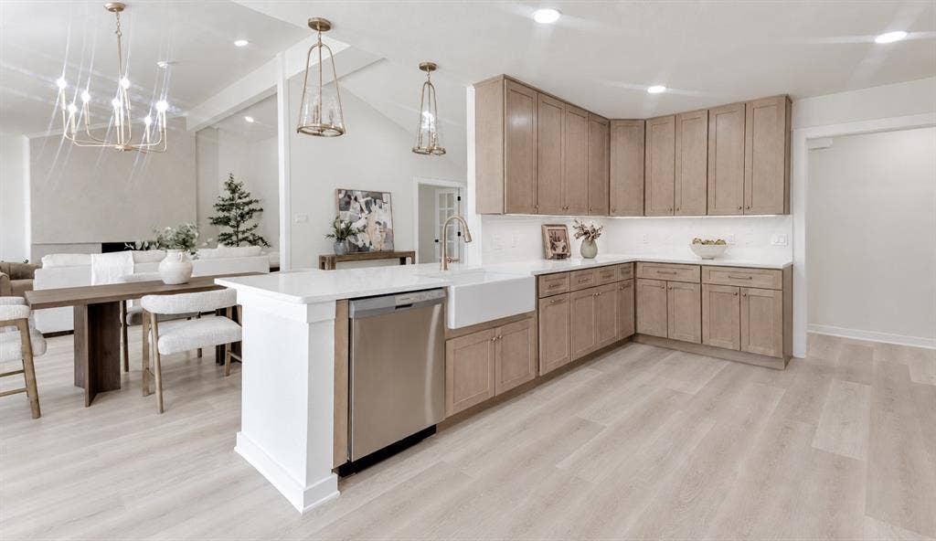 Wide Open-concept kitchen featuring light wood-finish flooring, white quartz countertops, a large farmhouse sink, and stainless steel appliances