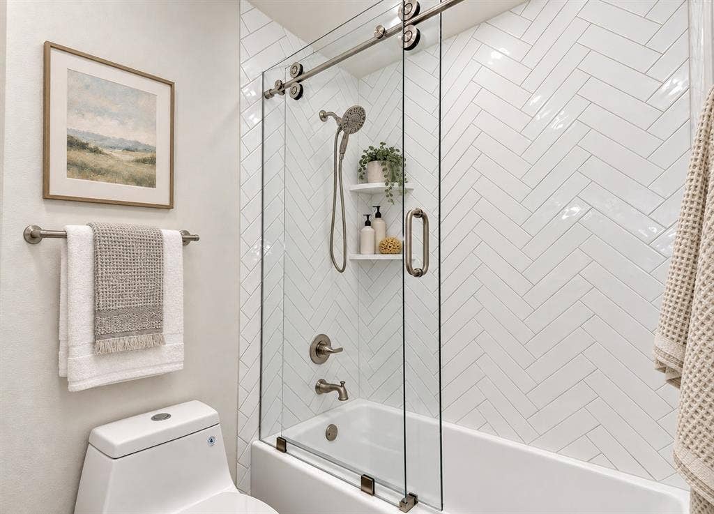 Herringbone tile shower surround, integrated bathtub, sliding glass shower door and a recessed shower shelf