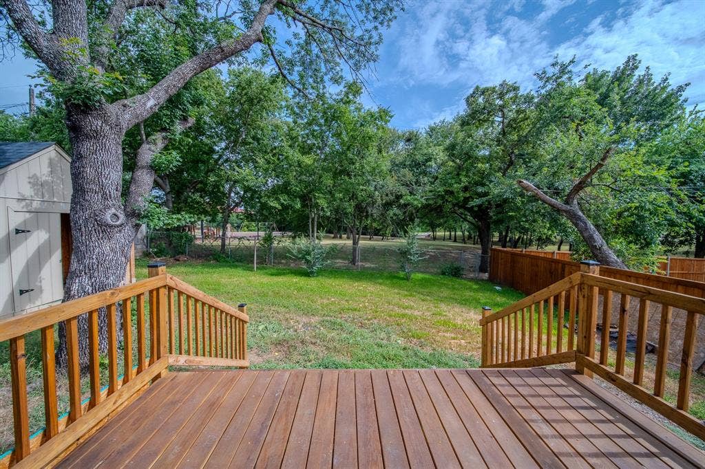 Spacious backyard featuring a large wood-finish deck with railings, an expansive lawn, mature shade trees, and a privacy fence
